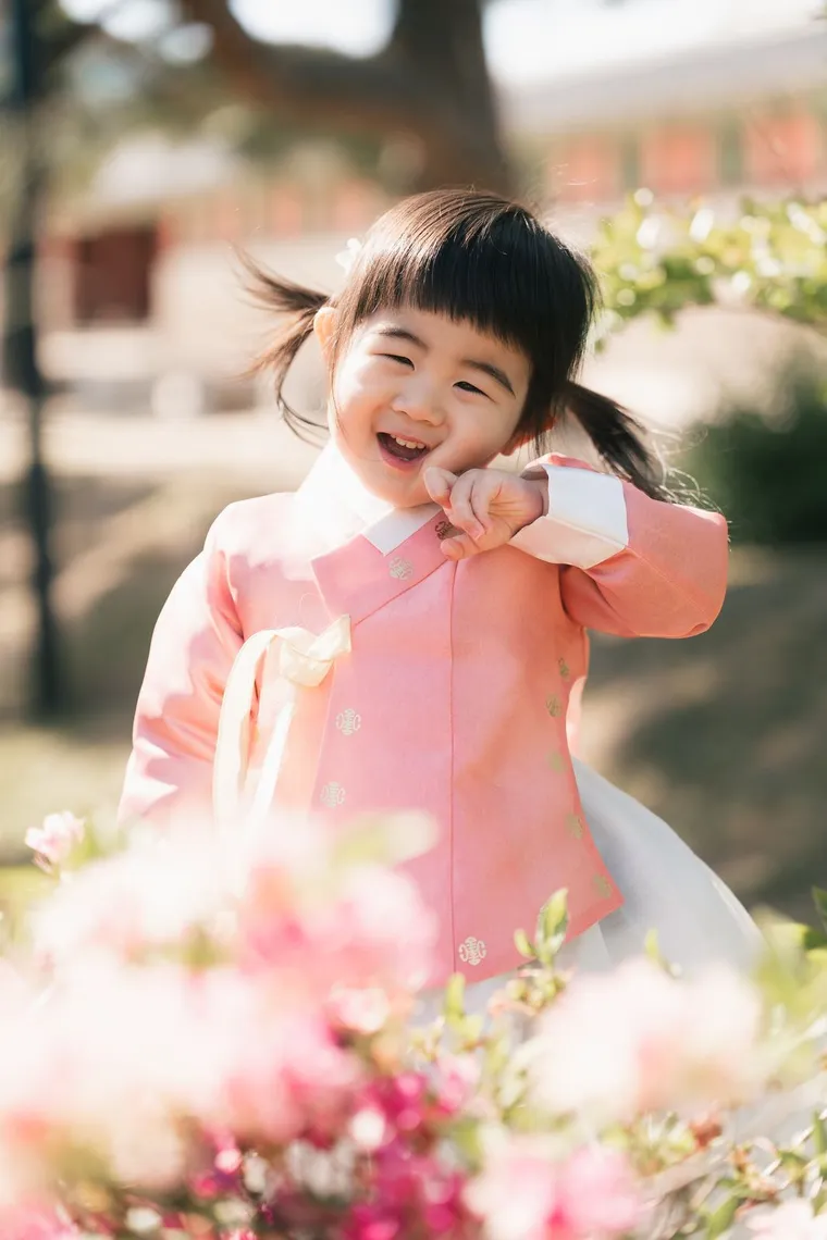 Small child in a pink hanbok laughing among spring blossoms