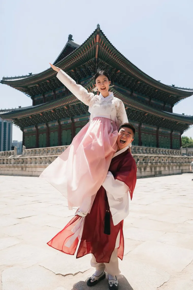 Child in a pink hanbok riding on her father's shoulders in front of a palace hall