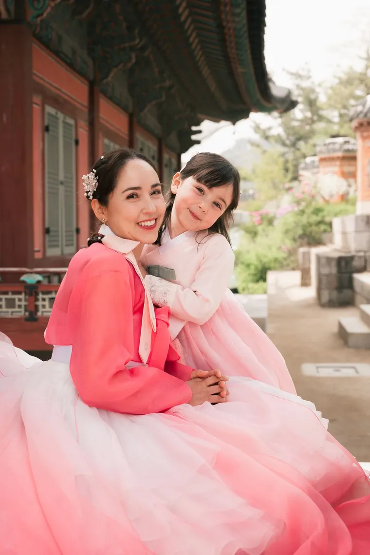 Mother and daughter in pink hanbok sitting together on a palace stair