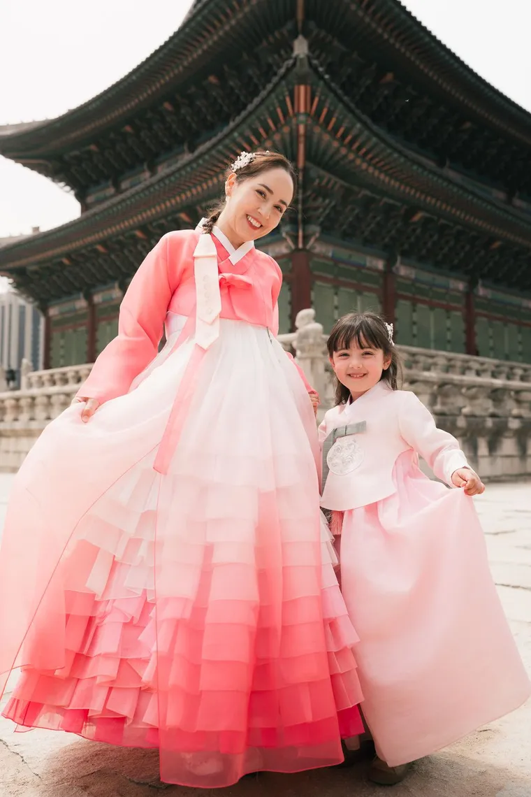 Mother and daughter in pink hanbok holding hands in front of a palace hall