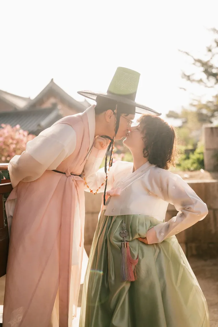Couple in pastel hanbok kissing beneath a palace wall