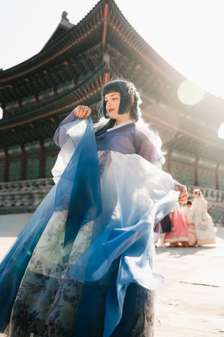 Woman in a blue hanbok twirling her skirt in a palace courtyard