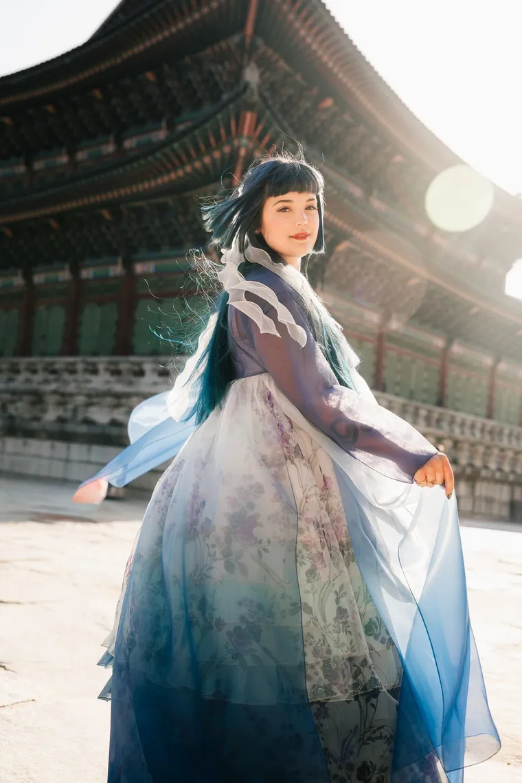 Woman in a blue hanbok turning with her skirt in motion under a palace roof