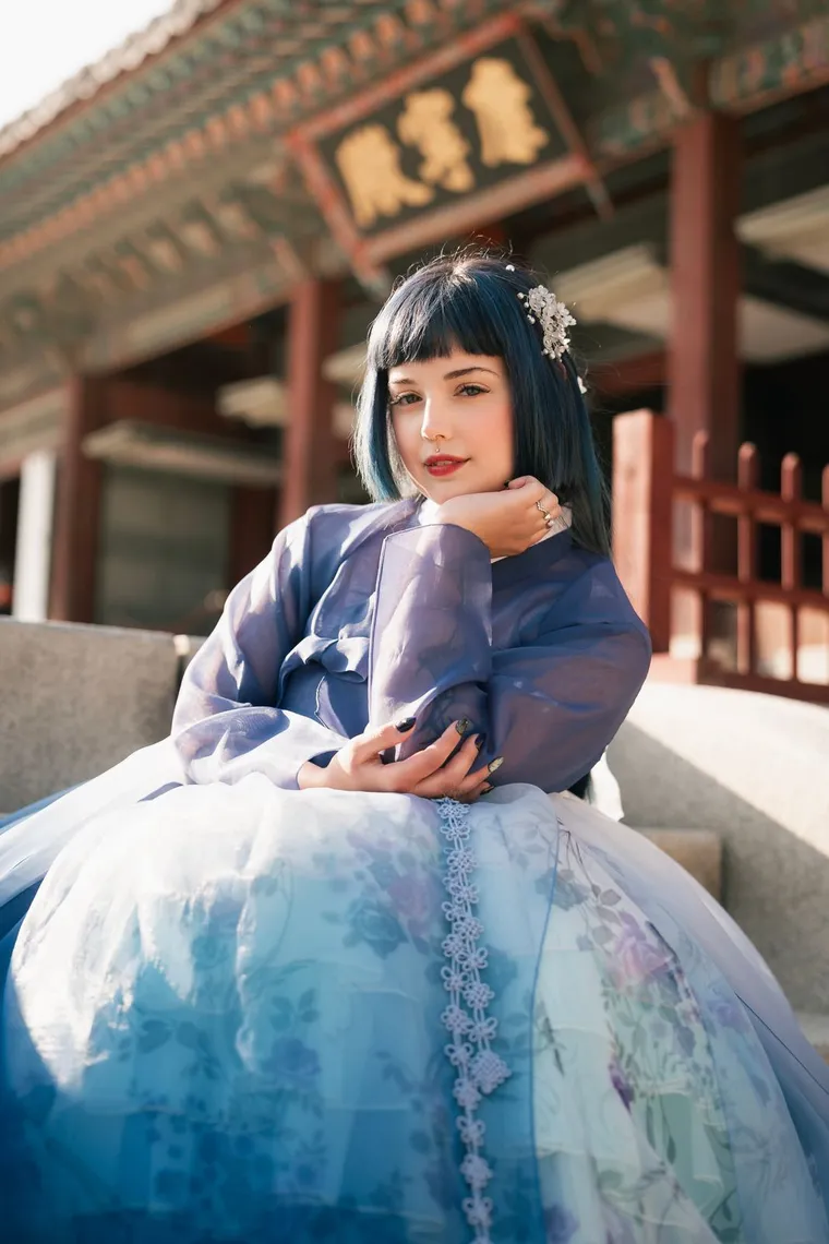 Woman in a blue hanbok seated on a palace stair in warm light