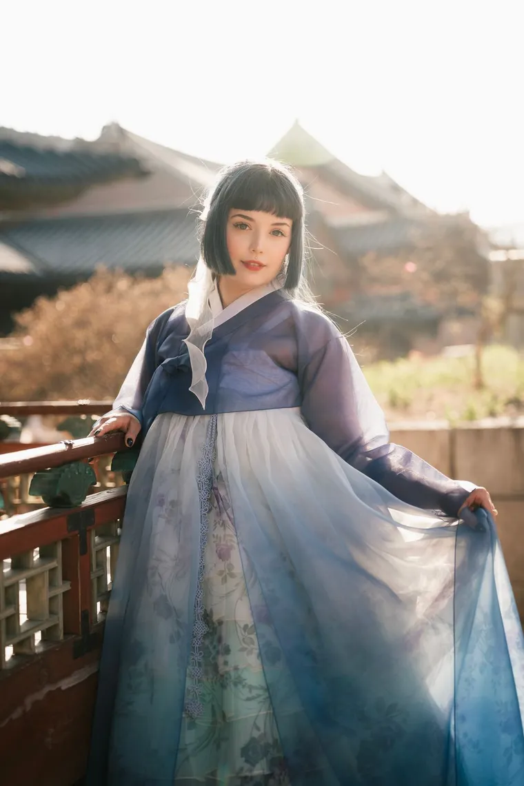 Woman in a blue hanbok leaning on a palace railing
