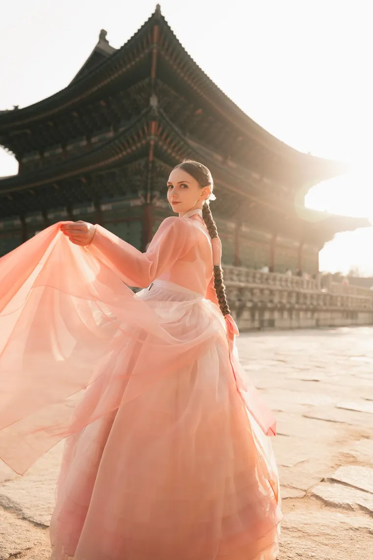 Woman in a pink hanbok twirling on a palace terrace