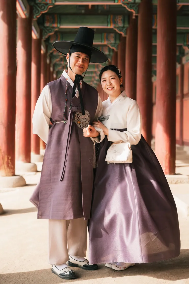 Couple in matching purple hanbok standing in a red-columned corridor