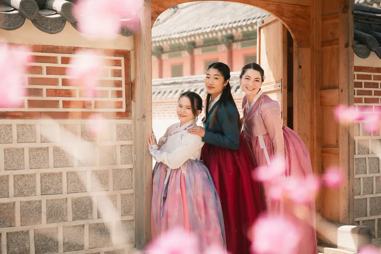 Three friends in hanbok framed by blossoms in a palace doorway