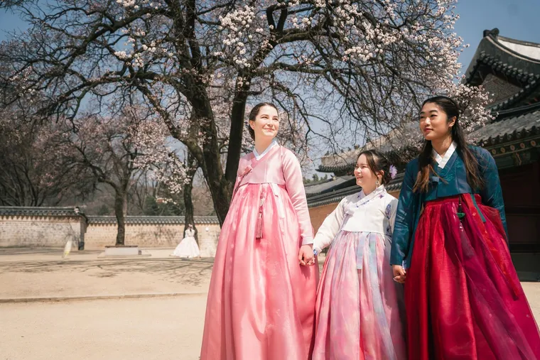 Three friends in hanbok under a blossoming tree in a palace courtyard