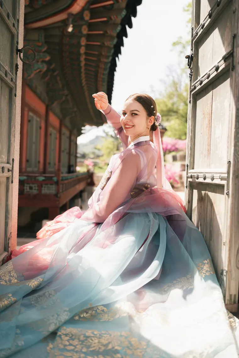 Woman in a lilac hanbok seated on a palace stair, laughing