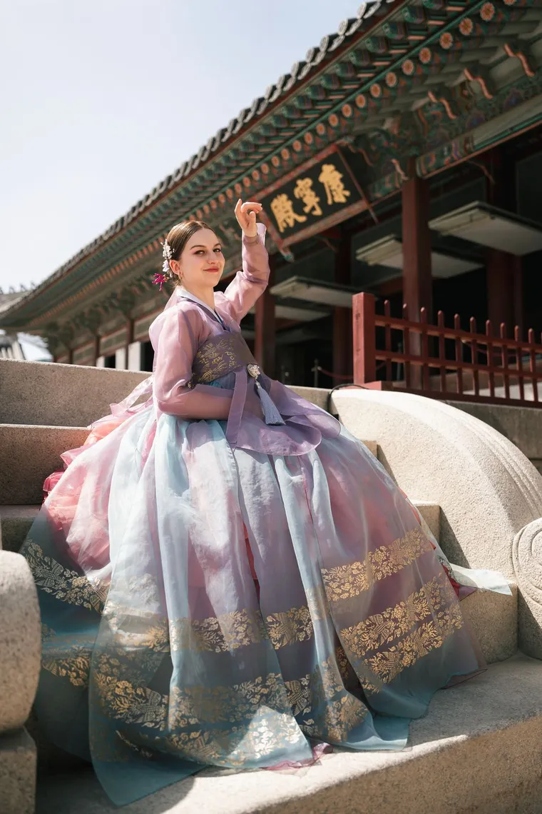 Woman in a lilac hanbok seated beneath a palace hall sign