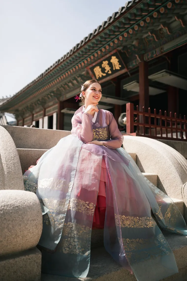 Woman in a lilac hanbok on a palace stair with her skirt spread