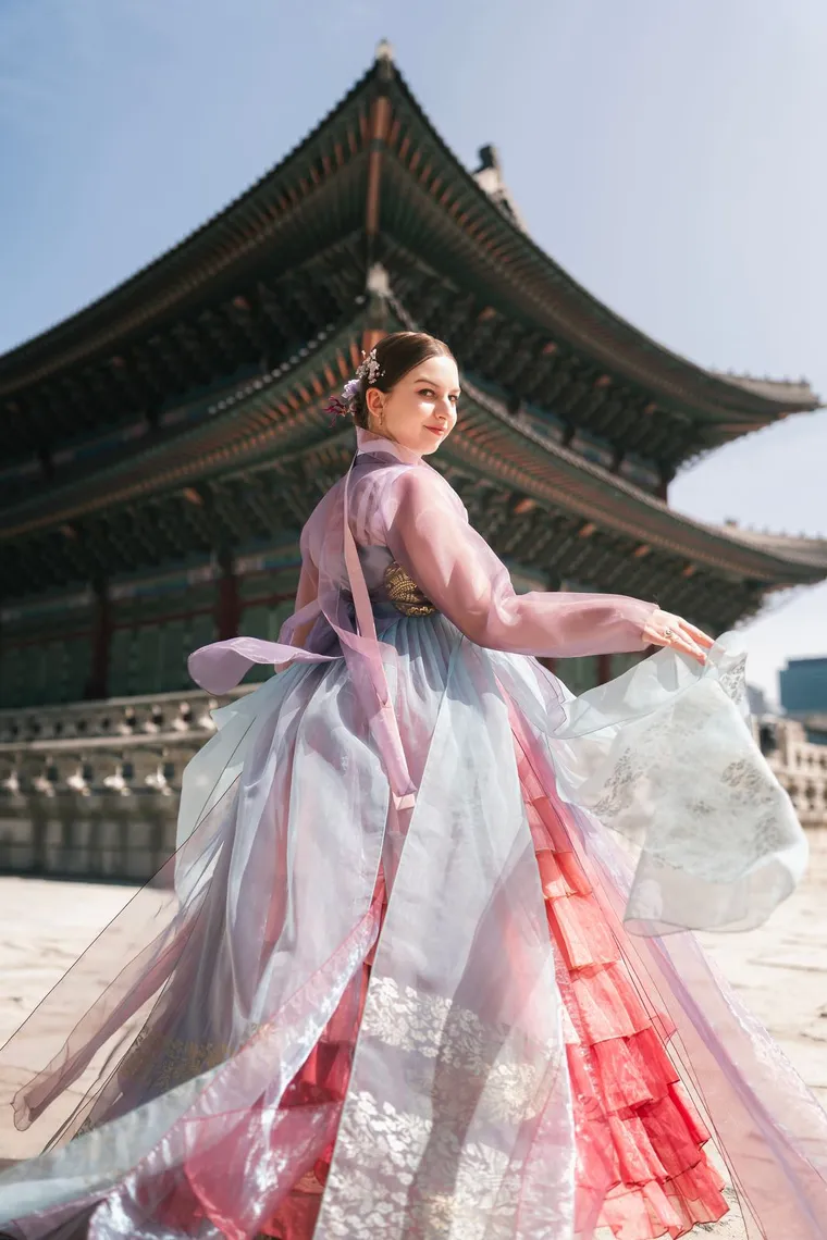 Woman in a lilac hanbok twirling in front of a palace hall