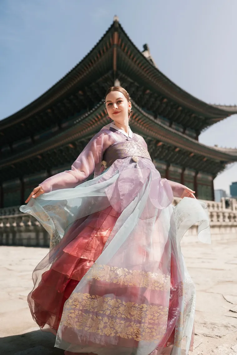 Woman in a lilac hanbok spinning with her skirt in motion in front of a palace hall